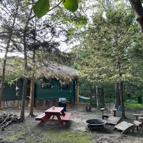 A cozy, wooden cabin nestled in a scenic setting with the sun setting behind it, emphasizing the rustic charm and peaceful atmosphere at Oak Meadow Ranch RV in Valley View, TX.