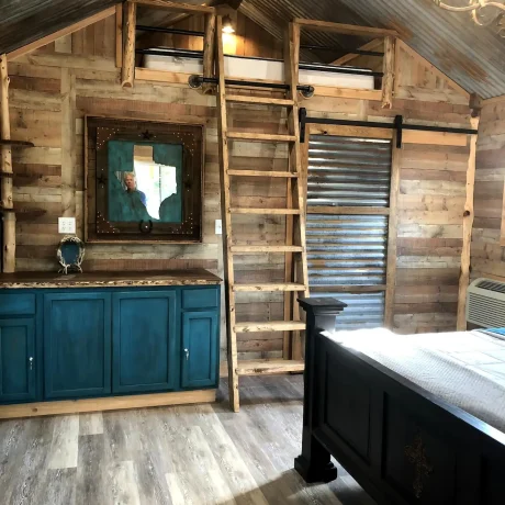 A cozy, wooden cabin nestled in a scenic setting with the sun setting behind it, emphasizing the rustic charm and peaceful atmosphere at Oak Meadow Ranch RV in Valley View, TX.