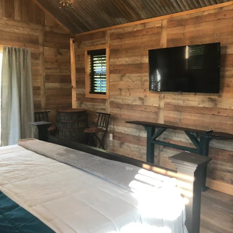 A cozy, wooden cabin nestled in a scenic setting with the sun setting behind it, emphasizing the rustic charm and peaceful atmosphere at Oak Meadow Ranch RV in Valley View, TX.