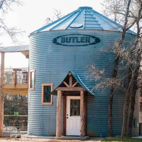 A cozy, wooden cabin nestled in a scenic setting with the sun setting behind it, emphasizing the rustic charm and peaceful atmosphere at Oak Meadow Ranch RV in Valley View, TX.