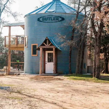 A cozy, wooden cabin nestled in a scenic setting with the sun setting behind it, emphasizing the rustic charm and peaceful atmosphere at Oak Meadow Ranch RV in Valley View, TX.